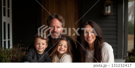 Happy family of four smiles warmly on their home's porch, showcasing family togetherness and happiness 131232417