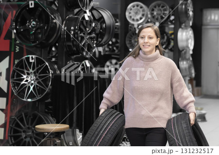 a young female car enthusiast carrying tires. She bought new tires to change her car shoes for the tire change season. maybe she is the seller and gives the tires to the buyer a young female car enthusiast carrying tires. She bought new tires to change her car shoes for the tire change season. maybe she is the seller and gives the tires to the buyer 131232517