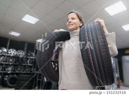 Woman carries tires at tire store in preparation for tire change season and makes a purchase for her vehicle Woman carries tires at tire store in preparation for tire change season and makes a purchase for her vehicle 131232518
