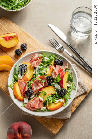 Fresh salad with peaches, arugula, feta, prosciutto and berries in a plate on a wooden board Fresh salad with peaches, arugula, feta, prosciutto and berries in a plate on a wooden board 131232630