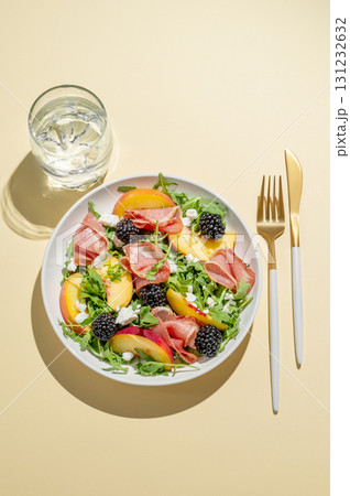 Fresh salad with peaches, arugula, feta, prosciutto and berries in a plate on a yellow background Fresh salad with peaches, arugula, feta, prosciutto and berries in a plate on a yellow background 131232632