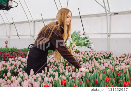 Female florist carefully arranging vibrant tulips in a greenhouse, surrounded by colorful blooms, showcasing the beauty of floral artistry and dedication to horticulture in a serene environment Female florist carefully arranging vibrant tulips in a greenhouse, surrounded by colorful blooms, showcasing the beauty of floral artistry and dedication to horticulture in a serene environment 131232937