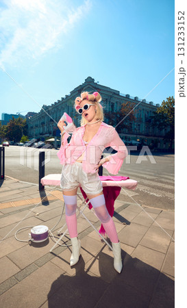 Playful stylish woman with pink curlers and retro outfit posing with iron outdoors 131233152