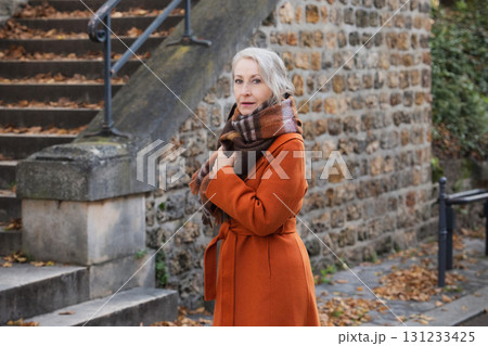 Grey-haired woman of sixty years old in a orange coat and a terracotta scarf Grey-haired woman of sixty years old in a orange coat and a terracotta scarf 131233425