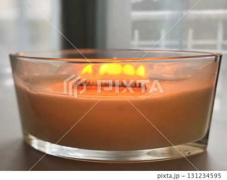 Large scented candle in glass jar burning in cozy autumn home interior, warm hygge atmosphere, aromatherapy Large scented candle in glass jar burning in cozy autumn home interior, warm hygge atmosphere, aromatherapy 131234595