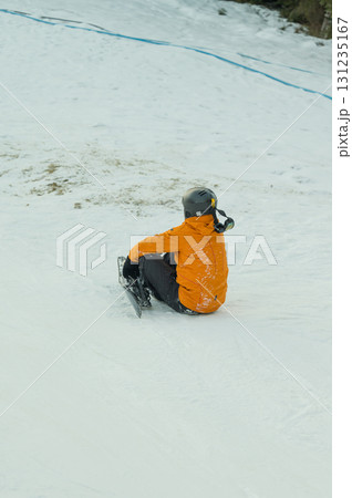 Bright orange jacket contrasts against the white snow as a lone sledder prepares for a thrilling ride down a winter slope at a mountain resort in early afternoon 131235167