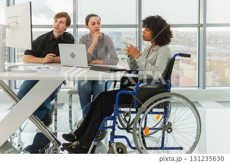 Teamwork brainstorm. Diverse multiracial colleagues woman in chair for people with disability working together. Group of people sitting in creative office discussing business. Young professional team Teamwork brainstorm. Diverse multiracial colleagues woman in chair for people with disability working together. Group of people sitting in creative office discussing business. Young professional team 131235630