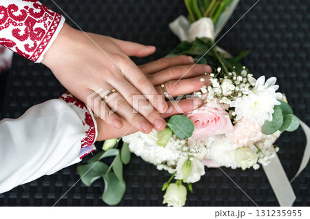 Newlywed couple's hands resting on a beautiful wedding bouquet. A symbol of love and commitment. Newlywed couple's hands resting on a beautiful wedding bouquet. A symbol of love and commitment. 131235955