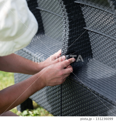 Assembling outdoor wicker furniture. Hands connect pieces. 131236099