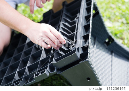 Assembling outdoor patio furniture. A person connects pieces of a gray plastic modular system. 131236165