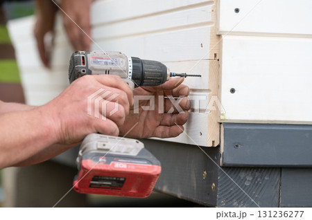The builder attaches the wall to the gazebo frame using screws and a screwdriver. The builder attaches the wall to the gazebo frame using screws and a screwdriver. 131236277