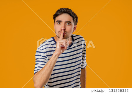 Handsome man with gesture of shhh, secret, silence, conspiracy, quiet, rumor concept. Smiling guy holding finger on lips, yellow studio background Handsome man with gesture of shhh, secret, silence, conspiracy, quiet, rumor concept. Smiling guy holding finger on lips, yellow studio background 131236335