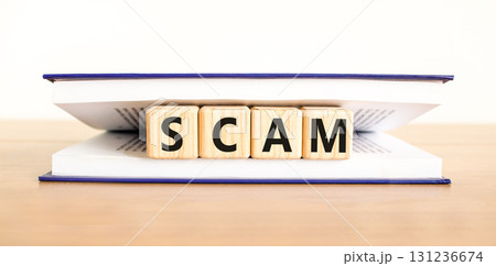 Scam symbol. Concept word Scam on beautiful wooden blocks in book. Beautiful wooden table white background. Business, lifestyle, support and scam concept. Copy space. Scam symbol. Concept word Scam on beautiful wooden blocks in book. Beautiful wooden table white background. Business, lifestyle, support and scam concept. Copy space. 131236674