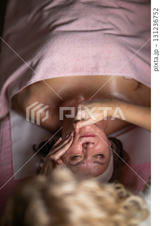Close up of a mature woman lying on a treatment bed with a towel while a professional therapist performs a relaxing chest massage. Spa wellness and beauty treatment concept highlighting relaxation 131236752
