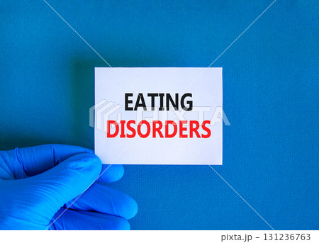Eating disorders symbol. Concept words Eating disorders on beautiful white card. Doctor's hand in blue medical glove. Beautiful blue background. Medical healthy lifestyle eating disorders concept. 131236763