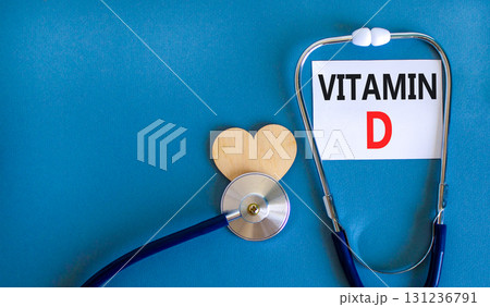 Vitamin D symbol. Concept words Vitamin D on beautiful white card. Wooden heart and stethoscope. Beautiful blue background. Medical healthy lifestyle Vitamin D concept. 131236791