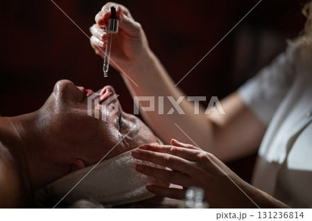 Close up of a mature woman lying in a spa while a therapist applies skincare serum with a dropper above her face. Beauty and wellness concept highlighting anti aging treatment, hydration, and holistic Close up of a mature woman lying in a spa while a therapist applies skincare serum with a dropper above her face. Beauty and wellness concept highlighting anti aging treatment, hydration, and holistic 131236814