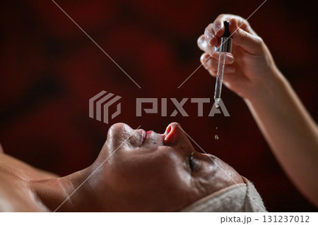 Close up of a mature woman lying in a spa while a therapist applies skincare serum with a dropper above her face. Beauty and wellness concept highlighting anti aging treatment, hydration, and holistic 131237012