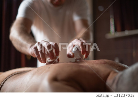 Close up of therapist applying cupping therapy on male clients back during wellness and rehabilitation treatment, traditional alternative medicine for relaxation and pain relief. 131237018