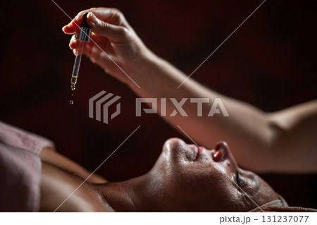 Close up of a mature woman lying in a spa while a therapist applies skincare serum with a dropper above her face. Beauty and wellness concept highlighting anti aging treatment, hydration, and holistic Close up of a mature woman lying in a spa while a therapist applies skincare serum with a dropper above her face. Beauty and wellness concept highlighting anti aging treatment, hydration, and holistic 131237077