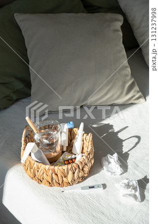 Wicker basket with medications, water glass and thermometer on white bedspread. Cold and flu treatment 131237998