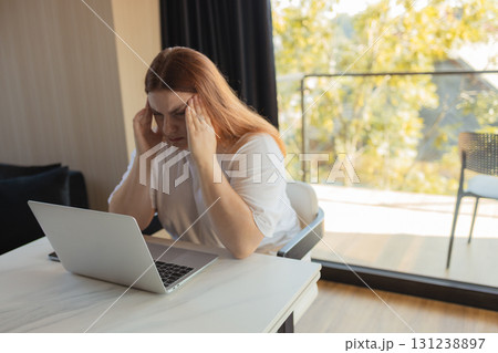 Tired woman holding head while working on laptop at home Tired woman holding head while working on laptop at home 131238897