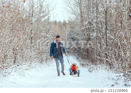 Dad pulling sled with his daughter on it in a winter forest 131238966