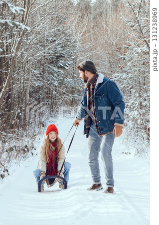 Dad pulling sled with his daughter on it in a winter forest 131238969