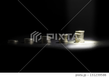 Front view of coins stacked at different heights with a spotlight highlighting the tallest coin, symbolizing success, leadership, financial growth, and achievement. Copy space included 131239586