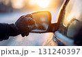 Hand in glove cleaning ice and snow from a frozen car mirror during a cold winter sunrise 131240397