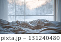Messy cozy bed with rumpled sheets near large window overlooking peaceful snowy winter landscape 131240480