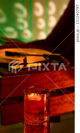 Crystal glass with red cocktail and cherry garnish beside glowing turntable Crystal glass with red cocktail and cherry garnish beside glowing turntable 131240797