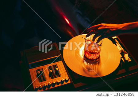 Hand adjusting cocktail glass on vinyl turntable in moody nightlife atmosphere 131240859