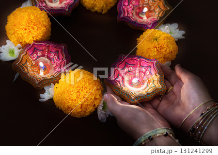 Hands holding Diwali candles with marigold flowers in a circle 131241299