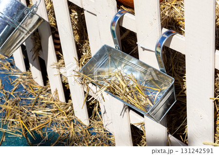 Rustic metal planter box and bucket overflowing with golden straw, adorning a white wooden fence, perfect for an autumn harvest display Rustic metal planter box and bucket overflowing with golden straw, adorning a white wooden fence, perfect for an autumn harvest display 131242591