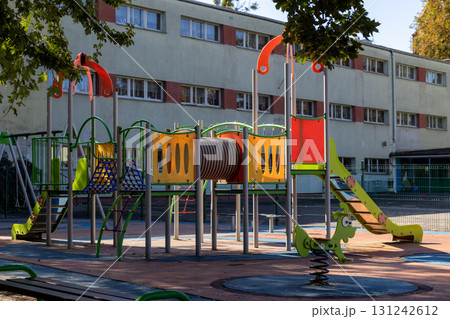 Colorful empty playground with modern equipment like a slide, tunnel, and climbing structure, designed for children's recreation and outdoor fun near a school building Colorful empty playground with modern equipment like a slide, tunnel, and climbing structure, designed for children's recreation and outdoor fun near a school building 131242612