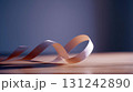 Pink satin ribbon lying on wooden surface with soft light and shadows, minimal composition with elegant and romantic mood 131242890