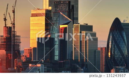 United Kingdom, London: Warm sunset light reflecting off glass facades of London skyscrapers, including The Gherkin, with construction cranes in view. Drone flight United Kingdom, London: Warm sunset light reflecting off glass facades of London skyscrapers, including The Gherkin, with construction cranes in view. Drone flight 131243937