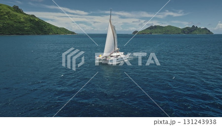 Fiji: Catamaran sailing blue ocean near tropical island on beautiful sunny day, offering perfect aerial view of dream vacation. Remote wild nature paradise, exotic summer travel. Drone flight Fiji: Catamaran sailing blue ocean near tropical island on beautiful sunny day, offering perfect aerial view of dream vacation. Remote wild nature paradise, exotic summer travel. Drone flight 131243938