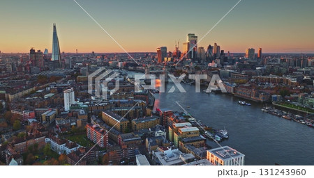 England, London: bright sunset colors reflecting on River Thames, Tower Bridge and The Shard rising in London's iconic skyline, captured from an aerial drone perspective. Popular iconic landmarks 131243960