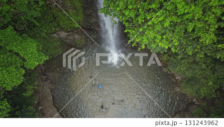 Fiji, Nadi Waterfall: picturesque waterfall cascades into a pool where tourists people swim and enjoy nature's beauty. Lush green tropical rainforest. Wild nature landscape. Drone flight 131243962