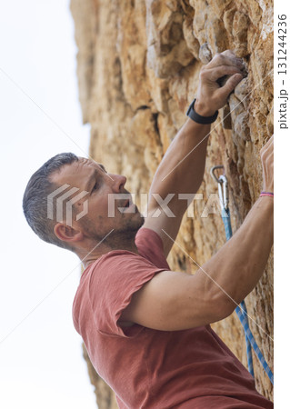 Man rock climbing a cliff, pulling himself up Man rock climbing a cliff, pulling himself up 131244236