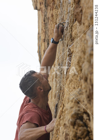 Man reaching for a quickdraw on a rock face Man reaching for a quickdraw on a rock face 131244238