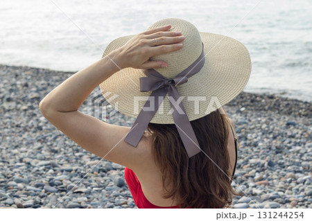 Attractive woman with long hair, wearing red bikini and straw hat, on the beach. Sea on the background. 131244254