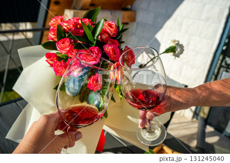 Close-up of two hands clinking wine glasses in a toast against a vibrant floral background. Perfect for romantic celebrations, lifestyle, and festive imagery. Close-up of two hands clinking wine glasses in a toast against a vibrant floral background. Perfect for romantic celebrations, lifestyle, and festive imagery. 131245040