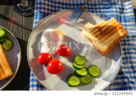 Healthy morning meal with eggs, cucumbers, tomatoes, toasts, and fruits served on a terrace table decorated with flowers and napkins. Healthy morning meal with eggs, cucumbers, tomatoes, toasts, and fruits served on a terrace table decorated with flowers and napkins. 131245043