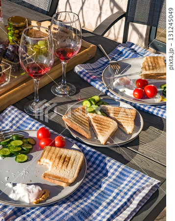 Rustic breakfast on a terrace including wine, homemade toasts with eggs and vegetables, fresh fruits, and blue checkered napkins. 131245049