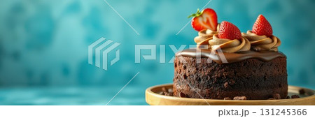 Chocolate cake topped with fresh strawberries and creamy frosting on a wooden platter against a blue backdrop 131245366
