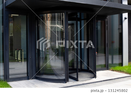 Modern revolving door of commercial building entrance with sleek glass design. Reflective surface highlights contemporary architecture, symbolizing accessibility and urban elegance in public spaces 131245802