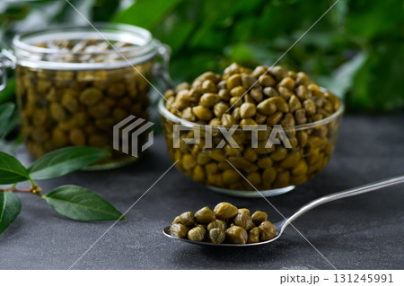 tasty pickled caper buds in a clear glass bowl on a black marble background, selective focus.Caper berry in a bowl . tasty pickled caper buds in a clear glass bowl on a black marble background, selective focus.Caper berry in a bowl . 131245991
